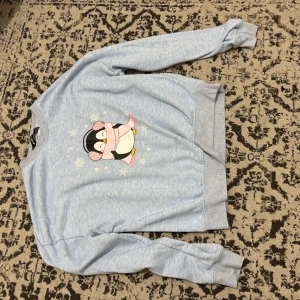 Ljusblå sweatshirt med pingvintryck - Säljer en ljusblå sweatshirt från H&M med ett gulligt pingvintryck på bröstet. Tröjan har långa ärmar, ribbade muddar och rund hals. Perfekt för dig som gillar söta motiv och vill ha en chill look.