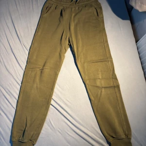 Olivgröna mjukisbyxor från Kappahl - Olivgröna mjukisbyxor från Kappahl med resår i midjan och muddar vid bensluten. Byxorna har två sidofickor och är tillverkade i mjuk bomullsmix som är skön att ha på sig. Perfekta för chill eller träning.