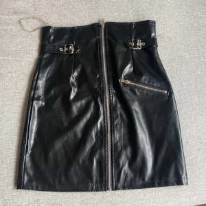 Svart skinnkjol,Boohoo,S - Snygg svart skinnkjol från Boohoo med framträdande dragkedja hela vägen framtill, två dekorativa bälten med spännen vid midjan och en snedställd ficka med dragkedja. Kjolen har en tight passform och är kort i modellen, perfekt för en edgy look.tror den är oanvänd. Eller använd 1 gång. Mycket bra skick hämtas i norsborg botkyrka eller fraktas så fort så möjligt pågrund av flytt.säljer allt hemma se gärna mina andra saker. Gör bra paketpris.