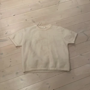 Beige stickad t-shirt från Gina Tricot - En beige stickad t-shirt från Gina Tricot i storlek 158/164. T-shirten har korta ärmar, rund halsringning och en loose passform. Perfekt för dig som gillar en enkel och stilren look med en mysig känsla.