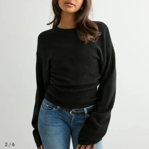 Svart stickad tröja med långa ärmar - En svart stickad tröja med rund hals och långa, lite oversized ärmar. Tröjan har en figurnära passform i midjan och är enkel men ändå snygg. Perfekt att matcha med jeans för en chill look.