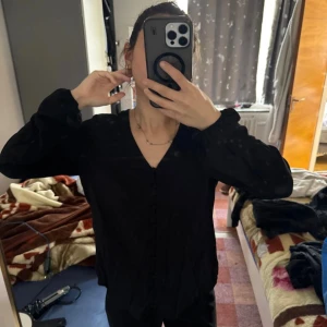 Svart blus med v-ringning från DeFacto - Säljer en svart blus från DeFacto i storlek S. Blusen har v-ringning, långa ärmar och knappar framtill. Den är lätt och skön, perfekt för dig som gillar stilrena och enkla plagg. Passar dig som vill ha en klassisk look med en modern touch.