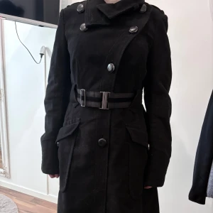 Svart trenchcoat från Mango Suit - Snygg svart trenchcoat från Mango Suit med bred krage, stora knappar och bälte i midjan. Skriv privat om ni har några frågor. 