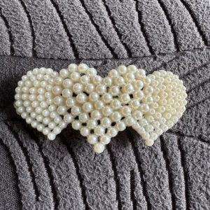 Hårklämma med pärlor i hjärtform - Superfin hårklämma dekorerad med vita pärlor formade som tre hjärtan. Klämman har en metallspänne på baksidan och ger en söt och romantisk vibe till din frisyr. Perfekt för att piffa upp håret med lite extra bling och charm.