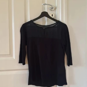Svart blus med transparent parti Lindex - Svart blus från Lindex i storlek S med trekvartsärm. Transparent meshparti upptill, rund halsringning och liten knappdetalj framtill. Använd ett fåtal gånger, i fint skick.