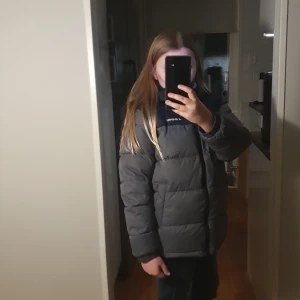 Grå och svart pufferjacka från Everest - Säljer en grå och svart pufferjacka från Everest med huva och dragkedja framtill. Jackan har en schysst quiltad look och logga på bröstet. Perfekt för kalla dagar och har en loose passform som ger en chill vibe.