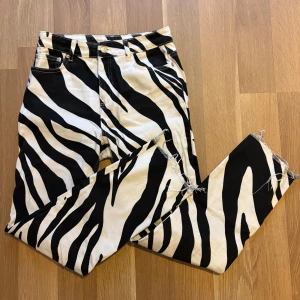 Zebramönstrade jeans från NA-KD - Snygga zebramönstrade jeans från NA-KD i svart och vitt. Byxorna har hög midja, raka ben och råa benslut för en trendig look. Tillverkade i kraftig bomull med klassisk femficksdesign och knappgylf.