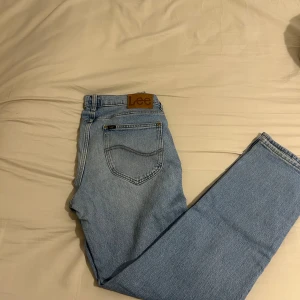 Ljusblå Lee jeans straight fit - Säljer ett par klassiska ljusblå jeans från Lee med raka ben och normal passform. Jeansen har fem fickor, bälteshällor och Lee-logga på bakfickan samt läderpatch i midjan. Perfekta för en avslappnad och stilren look.