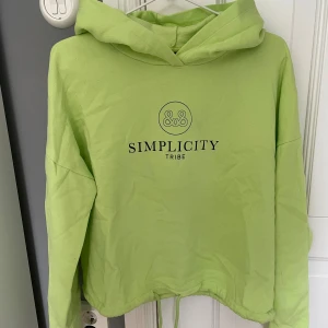 Ljusgrön hoodie från Gina Tricot - Säljer en ljusgrön hoodie från Gina Tricot med trycket 'Simplicity Tribe' på bröstet. Tröjan har huva, långa ärmar och dragsko nertill för en snygg passform. Perfekt för dig som gillar en chill och trendig stil.