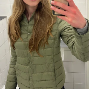 Olivgrön pufferjacka från H&M - Säljer en olivgrön pufferjacka från H&M i storlek 36. Jackan har ett quiltat mönster, tryckknappar framtill och lång ärm. Perfekt för kyliga dagar och har en clean, enkel look som är lätt att matcha med olika outfits.