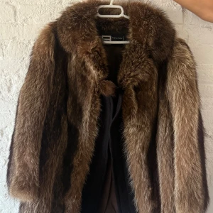 Vintage pälsjacka i äkta tvättbjörn – Alexandra Barcelona - Elegant vintagepäls från Alexandra Barcelona – Alta Peletería, tillverkad i Spanien. Klassisk, tidlös modell i äkta tvättbjörnspäls med vacker naturlig brun nyans och mjuk, lyxig känsla.   Jackan är i utmärkt vintageskick – ingen lukt, inga kala partier, fodret helt. Endast några få lösa stygn i fodret vid armhålan (enkelt att sy själv).  Storlek: ca M (passar S–M) Material: 100 % äkta tvättbjörn Färg: Brun/naturtoner Tillverkad och köpt i Spanien, skickas mot fraktkostnad.