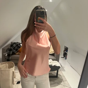 Ljusrosa satin linnetopp XS - Säljer en ljusrosa linnetopp i satin med halterneck och öppen rygg. Toppen har en snygg draperad framsida och tunna axelband. Perfekt för dig som gillar en stilren och chic look. Storlek XS.