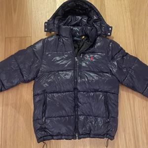 Mörkblå pufferjacka från Polo Ralph Lauren - Snygg mörkblå, glansig pufferjacka från Polo Ralph Lauren. Säljer den då den inte passar mig efter 2 vintrars försiktigt användande. Kan inte hitta en enda defekt på den, bara att höra av sig om man vill ha mer bilder eller diskutera pris☺️ Nypris: 6200kr