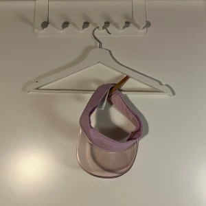 Lila solskärm med transparent skärm - Snygg lila solskärm med bred, transparent plastskärm och mjukt tygband runt huvudet. Perfekt för soliga dagar och ger en sportig vibe. Elastisk baktill för skön passform. Passar dig som vill sticka ut med en cool accessoar.