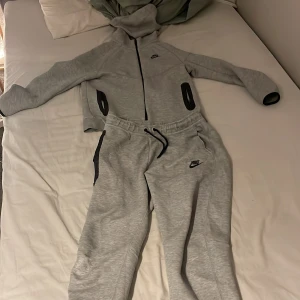 Grå nike tech - Säljer min gråa nike tech pågrund av att jag inte använder den längre. Passar som storlek XS och typ S och är 158-170 cm. Några slitningar på knä delarna av byxorna. Köpt för 2200 ungefär och säljer för 500 men kan defenetivt sänka priset.