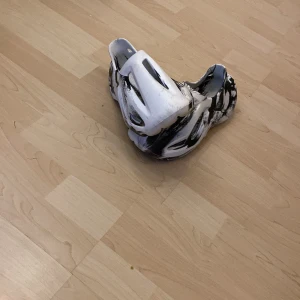 Svartvita foam sandaler i syntet - Unika sandaler i svartvitt mönster med coola utskärningar och chunky design. Tillverkade i lätt syntetmaterial som ger en futuristisk vibe. Perfekta för dig som vill sticka ut med en edgy stil och gillar bekväma skor med modern känsla.