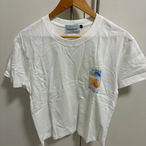 Vit t-shirt från Casablanca - Vit t-shirt från Casablanca med färgglad grafisk print på bröstet och ryggen. T-shirten har rund hals och korta ärmar. Tillverkad i mjuk bomull, perfekt för en avslappnad och trendig look.