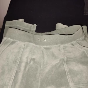 Gröna mjukisbyxor Juicy Couture S - Snygga gröna mjukisbyxor från Juicy Couture i storlek S. Byxorna har bred resår i midjan, stora fickor fram och bak, samt JC-broderi på ena fickan. Mjukt och glansigt material som känns lyxigt och skönt. Använda enstaka gånger, har tyvärr inga snören kvar🙏🏻
