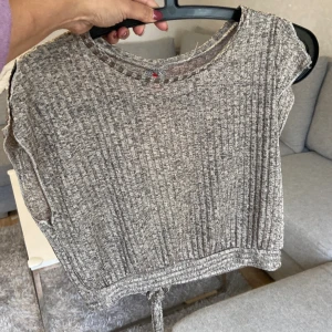 Beige ribbad topp med knyt - Säljer en beige ribbad topp med korta ärmar och rund hals. Toppen har ett snyggt knytband nedtill och är tillverkad i mjuk polyester med lite stretch. Perfekt för dig som gillar en chill och enkel stil med lite extra detalj i midjan.