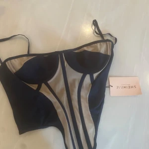 Mörkblå korsett-topp från SHEIN BAE - Snygg korsett-topp från SHEIN BAE i mörkblått med beige mesh-paneler och markerade sömmar framtill. Toppen har justerbara smala axelband och kupor med mesh-detaljer som ger en cool kontrast. Perfekt för dig som gillar trendiga och edgy plagg.