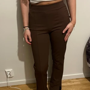 Bruna slitsade kostymbyxor - Snygga bruna kostymbyxor med hög midja och raka ben. XS men passar även en S. Byxorna har en tight passform upptill och slits framtill vid bensluten för en trendig look. Är lite flare mot slutet. Perfekta nu inför hösten när brunt är så populärt! 