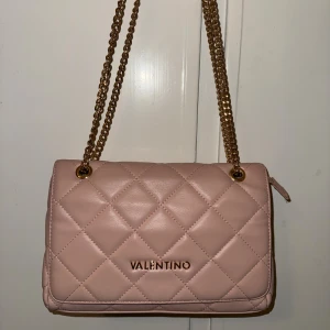 Rosa väska från Valentino - Supersnygg rosa axelväska från Valentino med quiltad design och guldfärgade kedjor. Väskan har dragkedja, innerfack och mjukt skinnliknande material. 