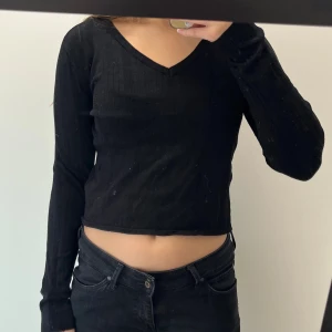Svart ribbad croppad långärmad topp - Svart långärmad topp från 157 i storlek S. Croppad modell med v-ringning och ribbad struktur som ger en snygg och enkel look. Perfekt att matcha med höga jeans eller kjol för en chill stil.