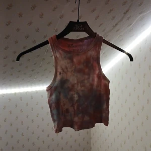 Croppad batikfärgad linnetopp XS - Säljer en croppad linnetopp från FSBN Sister i storlek XS. Toppen har ett coolt batikmönster i bruna, röda och blå toner. Modellen är ärmlös med rund hals och tillverkad i mjuk bomull. Perfekt för dig som gillar färg och vill sticka ut lite extra. Färgen är ljusare i verkligheten 