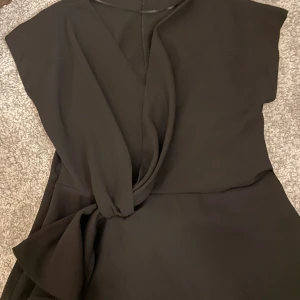 Svart omlotttröja  från Zara - Svart kortklänning från Zara med snygg omlottdetalj framtill och knyt i midjan. Klänningen har korta ärmar och en stilren, modern look som passar dig som gillar minimalistisk stil. Perfekt för dig som vill ha en enkel men chic outfit.