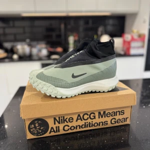 Nike ACG GORE-TEX sneakers grön/svart - Nike ACG sneakers med GORE-TEX, i ljusgrönt och svart med rutigt mönster och robust sula. Skorna har högt skaft, dragflik bak och lila detaljer under sulan. Perfekta för äventyr med vattentätt material och cool outdoor-vibe.