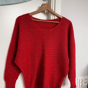 Röd stickad tröja med glittertråd - Snygg röd stickad tröja med glittriga inslag i garnet som ger en extra touch. Tröjan har långärmade ribbade muddar och ett luftigt, hålmönstrat stickat material. Rund halsringning och loose passform, perfekt för dig som gillar att sticka ut.