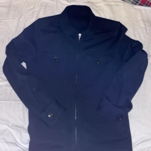 Mörkblå overshirt/cardigan från Hayden storlek  S - Snygg mörkblå overshirt från Hayden i storlek S. Jackan har hel dragkedja framtill, två bröstfickor med knappar och klassisk krage. Materialet är mjukt och känns som bomull, perfekt för lager-på-lager. Ärmarna har knappar vid mudden för extra stil.
