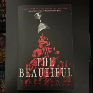 The Beautiful - En mystisk och lockande bok med ett mörkt omslag prytt av röda rosor och en elegant hjälm. Perfekt för dig som gillar spänning, romantik och en touch av det övernaturliga. Skriven av en bästsäljande författare.