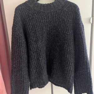 Mörkgrå stickad tröja med grov struktur - Säljer en mörkgrå stickad tröja med grov och mysig struktur. Tröjan har en rund hals och långa ärmar, perfekt för kyliga dagar. Passformen är loose och den har ribbade detaljer vid halsen. En enkel men snygg tröja som funkar till många stilar.