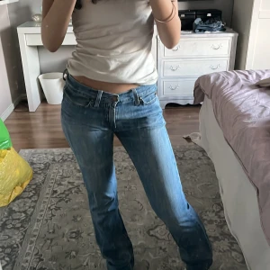 Lågmidjade blå jeans bootcut - Säljer ett par klassiska blå jeans med låg midja och bootcut-silhuett. Jeansen har fem fickor, snygga slitningar och är tillverkade i äkta denim. Perfekta för dig som gillar en avslappnad och tidlös look. Super sköna jeans.