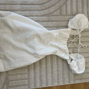 Vit kort klänning med puffärm - Supersöt vit kort klänning med puffiga ärmar och snörning i ryggen. Klänningen har en romantisk vibe med rynkad byst och offshoulder-design. Perfekt för varma dagar och somriga tillfällen.