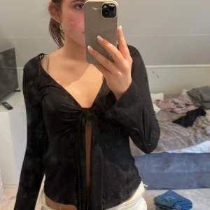 Svart omlottopp från Gina Tricot XS - Svart långärmad omlottopp från Gina Tricot i mjukt, stretchigt material. Toppen har djup v-ringning och knyt framtill som ger en snygg detalj. Perfekt att styla med jeans eller kjol för en trendig look.