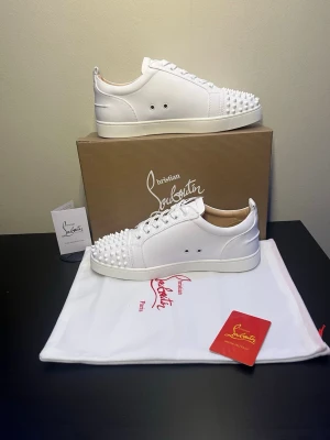 Christian Louboutin Skor - Säljer ett par vita Christian Louboutin Lou Spikes sneakers i skinn med ikoniska nitar på tån och klassisk röd sula. Skorna har snörning, rund tå och platt sula. Kommer med originalkartong, dustbag och certifikat. Perfekta för dig som vill sticka ut med exklusiv stil. Priset är diskuterbart vid snabb affär