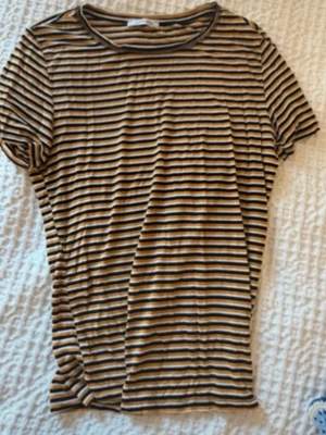 Randig t-shirt från Zara Trafaluc - Säljer en kortärmad t-shirt från Zara Trafaluc med tunna svarta, vita och senapsgula ränder. T-shirten har rund halsringning och är i mjuk bomull som känns skön mot huden. Perfekt till jeans eller kjol för en avslappnad look. Strl M