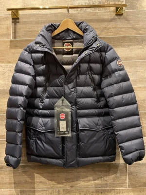 Colmar jacka(ny) - Säljer en svart pufferjacka från Colmar med hög krage, två bröstfickor med dragkedja och två stora fickor med lock. Jackan har en clean look med diskret logga på ärmen och quiltad design. Perfekt för kalla dagar och riktigt snygg till streetwear.