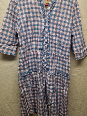 Blårutig klänning Tommy Hilfiger M - Supersöt blårutig klänning från Tommy Hilfiger i bomull. Modellen har knappar framtill, snörningsdetalj och volang längs med bröstet. Trekvartsärm och avslappnad passform. Perfekt för dig som gillar en chill men ändå stilsäker look.