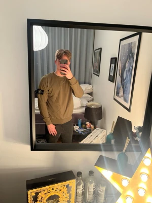 Olivgrön sweatshirt från Stone Island - Säljer en olivgrön sweatshirt från Stone Island med klassisk logotyp-patch på vänster ärm. Tröjan har rund hals, ribbade muddar och är tillverkad i mjuk bomull. Perfekt för dig som gillar streetwear och vill ha en clean look.