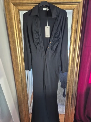 Svart byxdress från Giorgia Paris - Snygg svart byxdress från Giorgia Paris med långa ärmar, krage och djup v-ringning med knappar. Byxdressen har rynkade detaljer vid bysten och vida ben. Tillverkad i ett mjukt, stretchigt material som ger en bekväm passform.