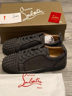 Christian Louboutin gråa sneakers med nitar - Grymma gråa sneakers från Christian Louboutin med gråa nitar på tån och klassisk röd sula. Skorna är i mocka med snörning och har en clean, lyxig vibe. Öppen för frågor, pris är ej hugget i sten