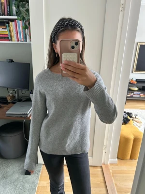 Grå stickad tröja från Vero Moda - Mysig grå stickad tröja från Vero Moda i storlek S. Tröjan har rund halsringning, långa ärmar och ribbade muddar vid ärmslut och nederkant. Perfekt för lager-på-lager under kyliga dagar.