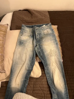 Coola jeans från G-Star - Säljer ett par ljusblå jeans från G-Star RAW, modell GS01. De har en tvättad och sliten look med färgstänk och patchdetaljer på framsidan