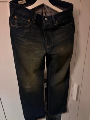 Levi's 501 jeans mörkblå W32 L30 - Klassiska Levi's 501 jeans i mörkblå tvätt med raka ben och knappgylf. Perfekta för dig som gillar tidlös denimstil och vill ha ett par slitstarka jeans i bomull. Slitningen har en smuts/dusty nyans.