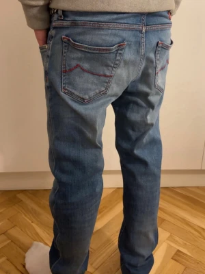 Jacob Cohen style 622 blå jeans med röd söm - Snygga blå jeans från Jacob Cohen med coola röda sömmar och detaljer på fickorna. Jeansen har en klassisk femficksdesign, normal passform och är tillverkade i mjukt bomullsmaterial. Märkespatch i rött på baksidan och riktigt fräsch tvätt överlag. Handgjorda i Italien och perfekt passform. Modellen är 175 och väger 63kg. Pris kan diskuteras.