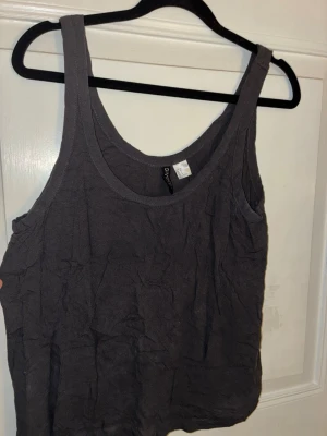 Mörkgrå linnetopp från Divided H&M - En enkel och loose mörkgrå linnetopp från Divided H&M. Toppen är ärmlös med breda axelband och rundad halsringning. Perfekt till sommaren och lätt att matcha med olika stilar. Materialet känns mjukt och luftigt.