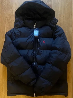 Svart pufferjacka från Polo Ralph Lauren - Svart pufferjacka från Polo Ralph Lauren med huva och tvåvägsdragkedja. Perfekt för kalla dagar|                                                                         skriv vid funderingar                                                                Priset kan självklart diskuteras!!